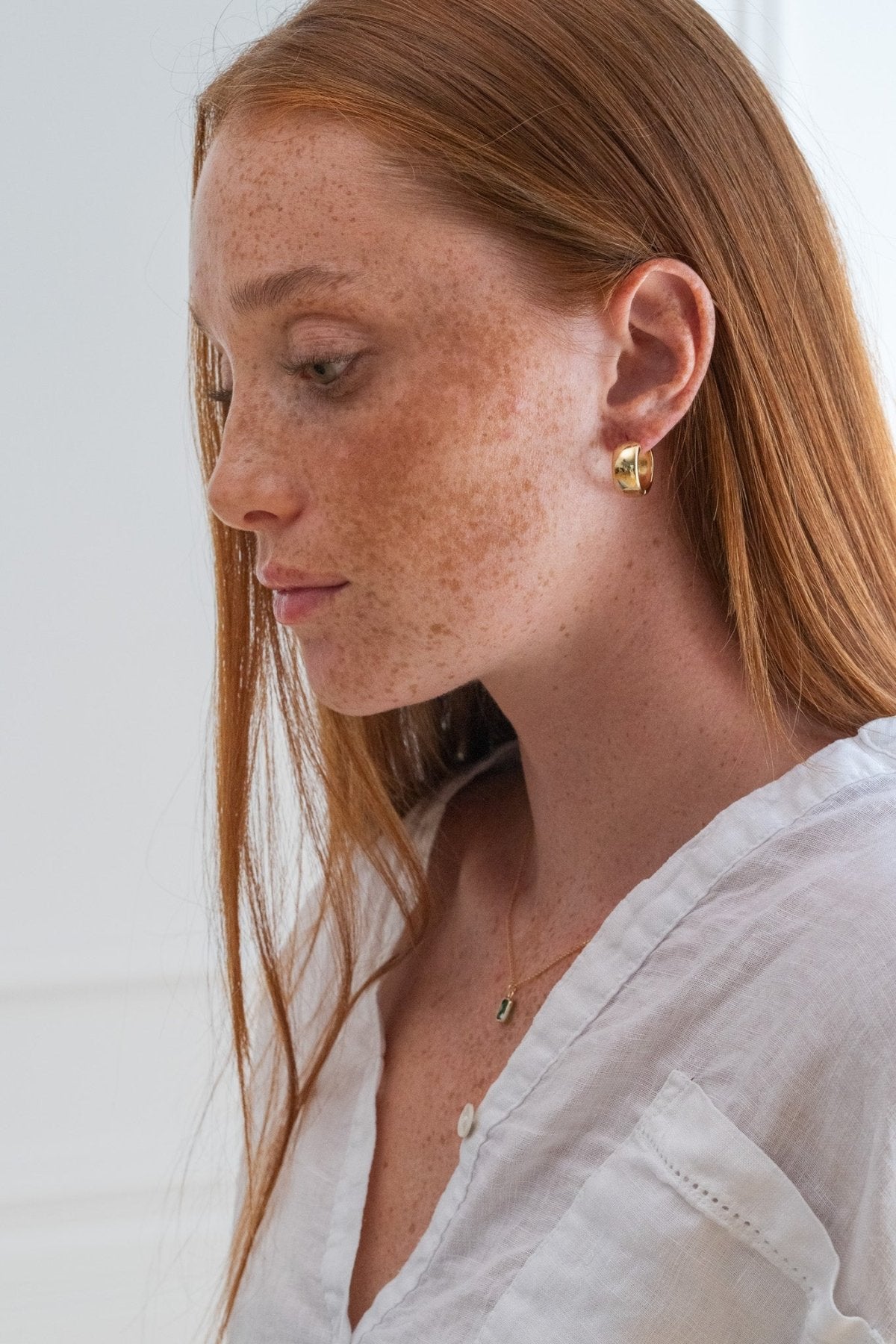 Woman with freckles wearing a white shirt and gold earrings against a light background