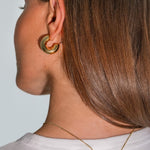 Close-up of a person wearing gold hoop earrings and a necklace with a white background