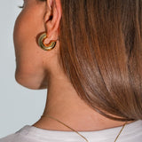 Close-up of a person wearing gold hoop earrings and a necklace with a white background