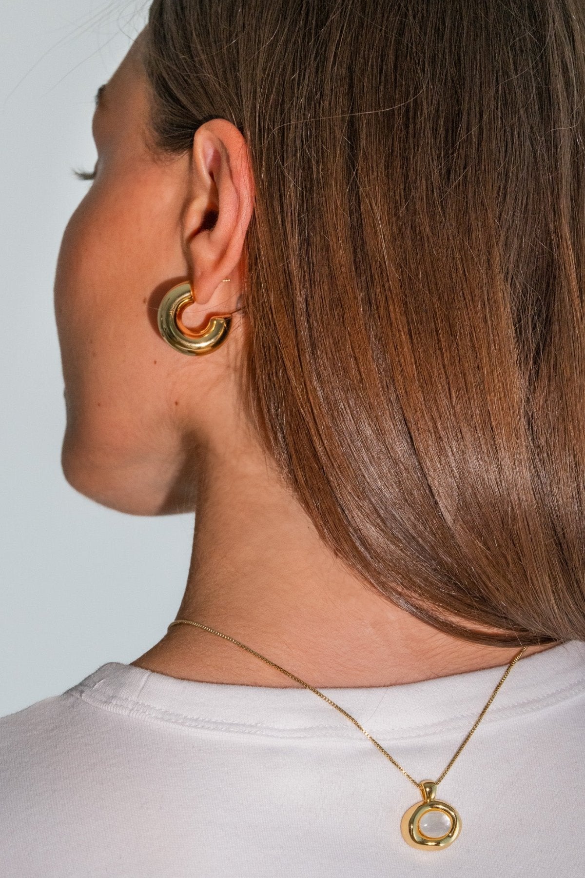 Close-up of a person wearing gold hoop earrings and a necklace with a white background