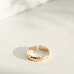 Gold flower patterned ring on a light gray surface with soft shadows