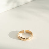 Gold flower patterned ring on a light gray surface with soft shadows