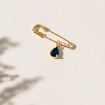 Close-up of a 'Something Blue' pin featuring a delicate blue gemstone set in an elegant gold frame. This charming accessory is the perfect wedding day keepsake, adding a personal and meaningful touch to the bride's attire.