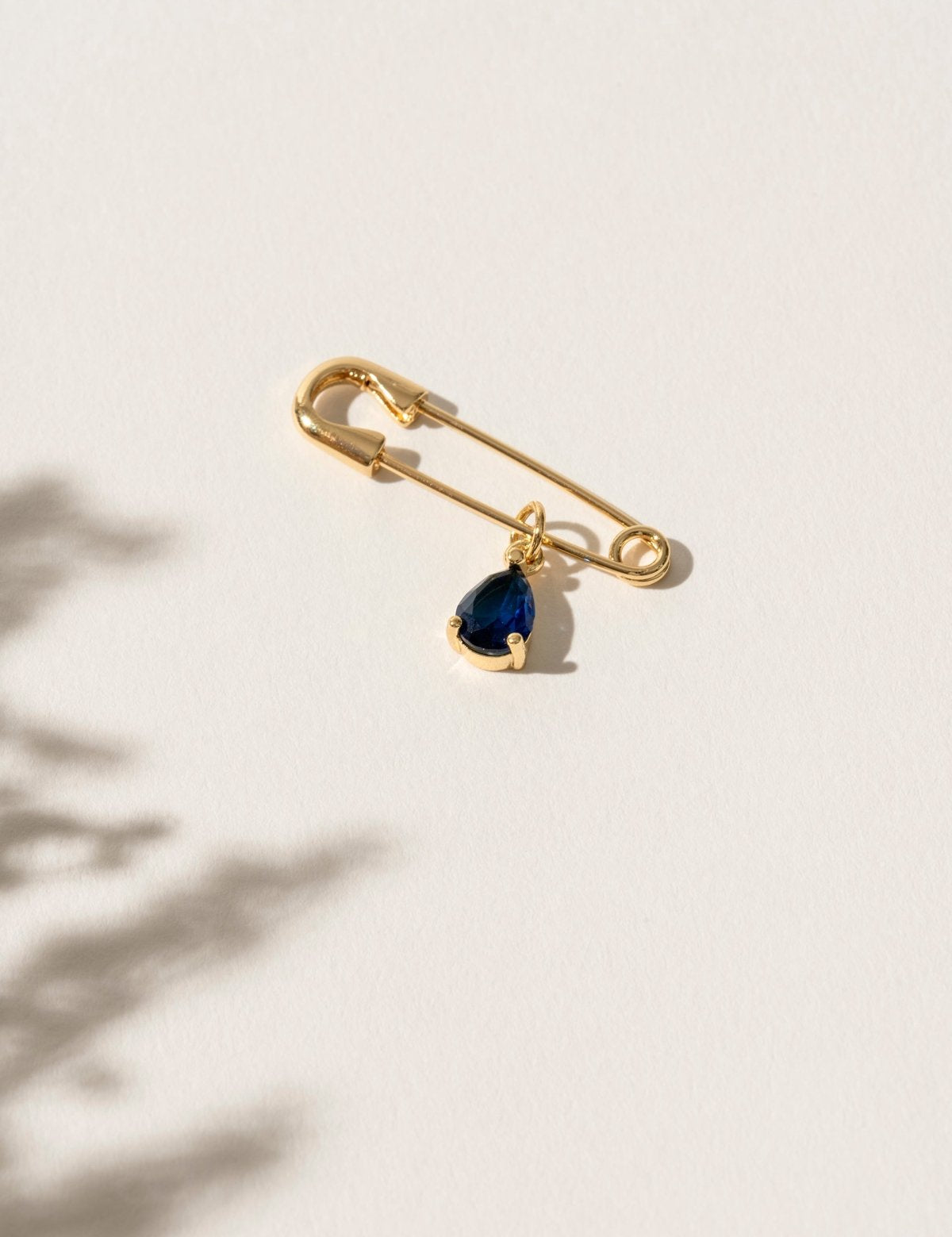 Close-up of a 'Something Blue' pin featuring a delicate blue gemstone set in an elegant gold frame. This charming accessory is the perfect wedding day keepsake, adding a personal and meaningful touch to the bride's attire.