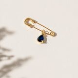 Close-up of a 'Something Blue' pin featuring a delicate blue gemstone set in an elegant gold frame. This charming accessory is the perfect wedding day keepsake, adding a personal and meaningful touch to the bride's attire.