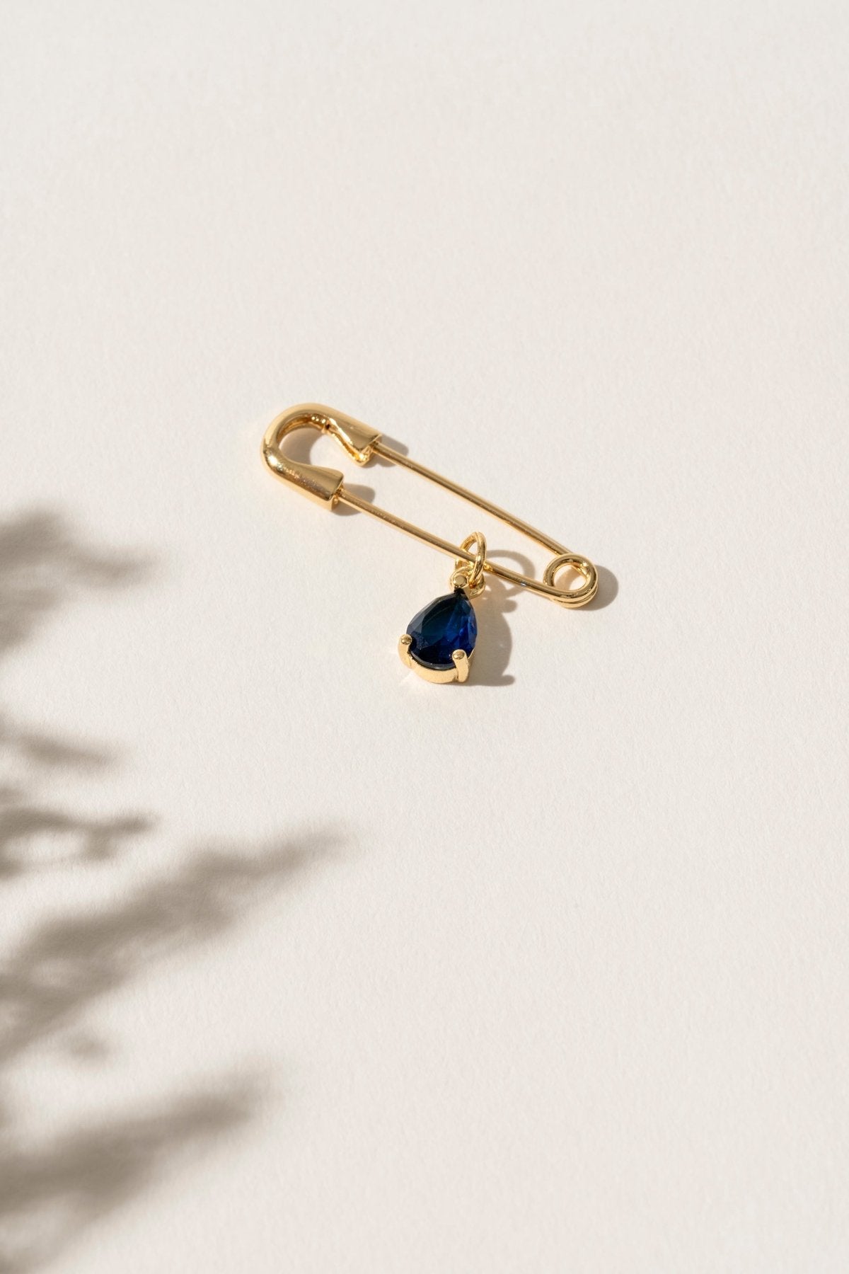 Close-up of a 'Something Blue' pin featuring a delicate blue gemstone set in an elegant gold frame. This charming accessory is the perfect wedding day keepsake, adding a personal and meaningful touch to the bride's attire.
