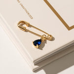Close-up of a 'Something Blue' pin in gold, featuring a subtle blue gemstone set in a sleek, timeless design. This elegant accessory adds a touch of tradition and charm to the bride’s ensemble, offering a meaningful and stylish detail on her wedding day.