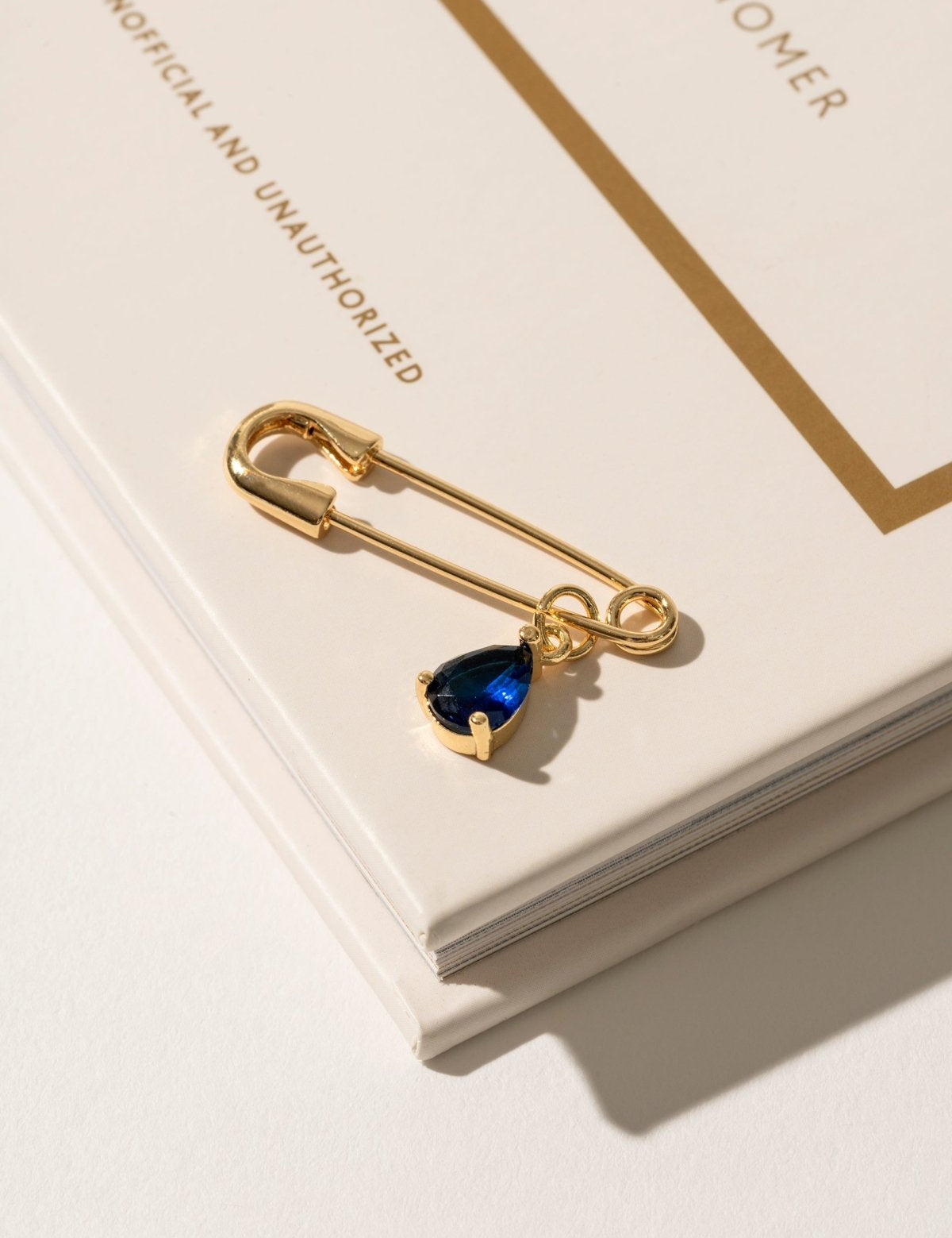 Close-up of a 'Something Blue' pin in gold, featuring a subtle blue gemstone set in a sleek, timeless design. This elegant accessory adds a touch of tradition and charm to the bride’s ensemble, offering a meaningful and stylish detail on her wedding day.