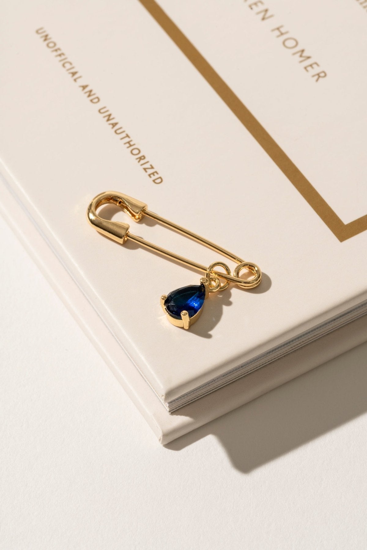 Close-up of a 'Something Blue' pin in gold, featuring a subtle blue gemstone set in a sleek, timeless design. This elegant accessory adds a touch of tradition and charm to the bride’s ensemble, offering a meaningful and stylish detail on her wedding day.